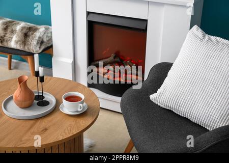 Table basse avec tasse de thé, verseuse et bougies dans le salon Banque D'Images