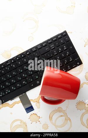 Une tasse de café rouge est brocartée sur un clavier d'ordinateur Banque D'Images