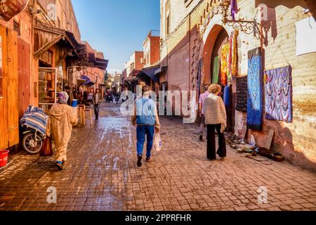 Marrakech, Maroc - 19 octobre 2015. Les touristes et les habitants marchent le long d'une rue dans le souk de la vieille ville tôt le matin, alors que les magasins ouvrent pour la journée. Banque D'Images