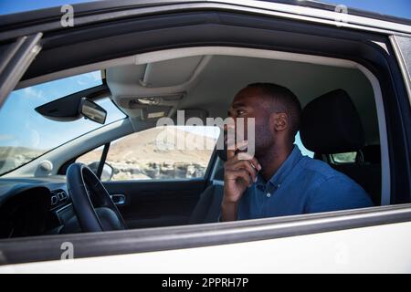 Un homme afro-américain avec une expression réfléchie assis dans sa voiture Banque D'Images