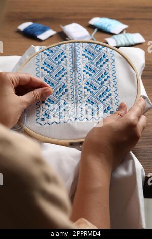 Femme brodant une chemise blanche avec fil bleu sur une table en bois, gros plan. Vêtements nationaux ukrainiens Banque D'Images