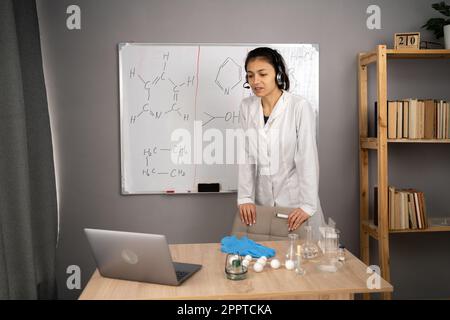 Enseignement à distance. Professeur d'école enseignant la chimie en ligne à partir de la salle de classe. Femme portant un casque sans fil lors d'une réunion virtuelle, ayant un appel vidéo Banque D'Images