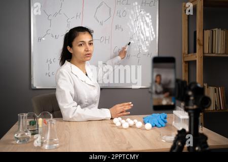 Femme enseignant faisant la vidéo conférence enseignement de la chimie en ligne pointant sur le tableau noir avec des formules à la maison. E-enseignement et blog éducatif Banque D'Images