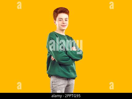 Modèle enfant en sweat-shirt vert posant avec les bras croisés sur fond jaune en studio de mode Banque D'Images