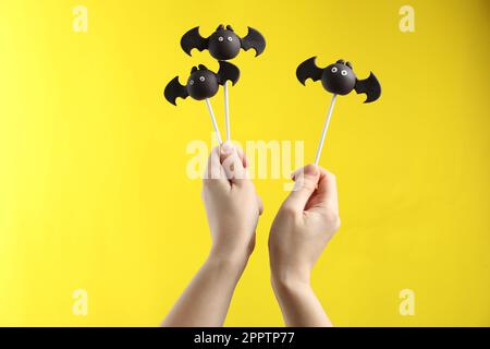 Femme avec de délicieux gâteaux en forme de chauve-souris sur fond jaune, gros plan. Fête d'Halloween Banque D'Images