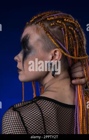 Tête de jeune femme avec horreur scène noire maquillage peint sur le visage et couleur orange Dreadlocks coiffure. Studio a réalisé un portrait spectaculaire sur le bleu b. Banque D'Images