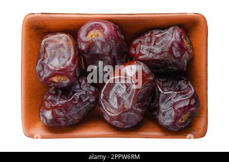 Dates sèches dans un bol en argile isolé sur blanc plat vue sur la pose Banque D'Images