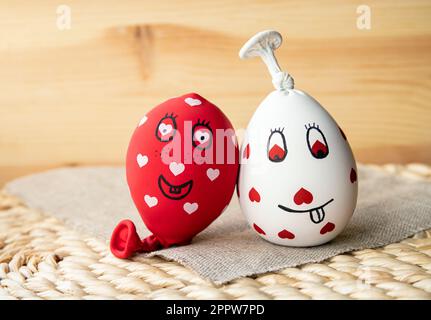 Deux boules de stress sensorielles maison amusantes, faites de ballons et remplies de farine. Boules rouges et blanches avec coeurs et visages drôles dessinés. Banque D'Images