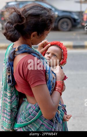 Une jeune mendiante à Mumbai, en Inde, porte son petit garçon qui la regarde avec une intensité ou un sérieux enfantin Banque D'Images