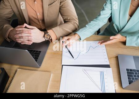 vue rognée d'une femme pointant vers des analyses d'entreprise à proximité de collègues et d'ordinateurs portables au bureau, image de stock Banque D'Images