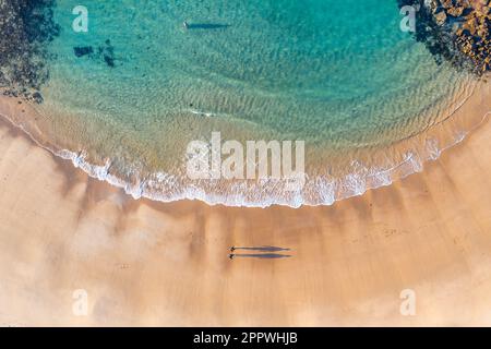 Vue aérienne d'une baie océanique calme avec eau turquoise et deux personnes marchant le long de la plage de sable à Cape Paterson à Victoria, en Australie Banque D'Images