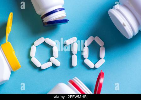 Coenzyme de la vitamine Q10. Pilules blanches formant la forme à Q10 signes et bouteilles en plastique sur fond bleu. Banque D'Images