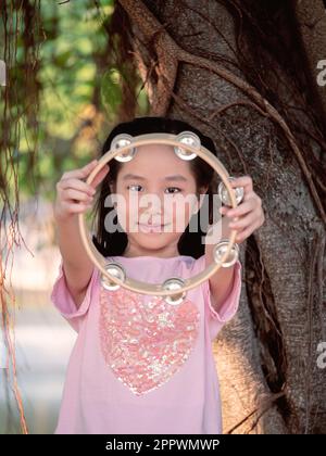 Petite fille asiatique jouer le tambourin, dans le jardin sous le grand arbre Banque D'Images