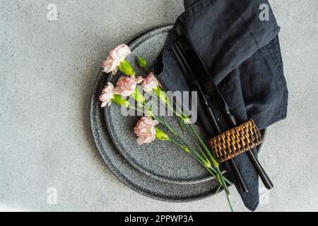 Placez le décor avec de la vaisselle grise et des fleurs de carnation roses Banque D'Images