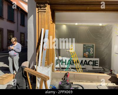 Ribeauville, France, 22 septembre 2022 : un travailleur adulte à l'extérieur d'une pharmacie répare sa façade, tandis que les acheteurs à l'intérieur recherchent des fournitures médicales et p Banque D'Images