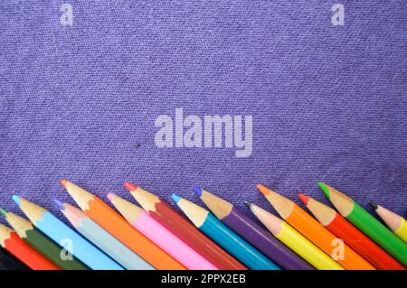 Crayons multicolores, lumineux et colorés situés à un angle de dessous et un espace libre pour votre texte sur fond violet. Banque D'Images