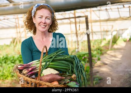 Portrait d'une agricultrice mûre souriante tenant un panier de légumes frais à la ferme Banque D'Images