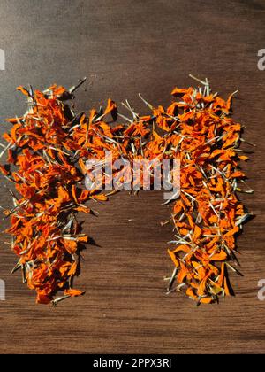 La lettre « M » est écrite avec des fleurs/graines de Marigold séchées sur une table en bois Banque D'Images