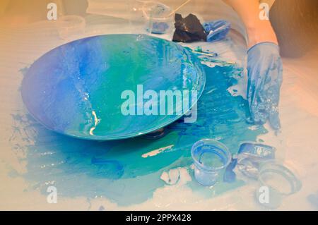 Un homme dans un gant bleu peint magnifiquement dessine une résine multicolore bleu acrylique un plateau rond fait maison. Banque D'Images