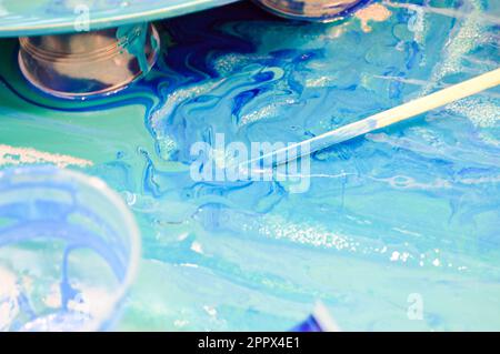 Le processus de création d'un modèle moderne abstrait fait maison peint avec un pinceau de résine multicolore bleu acrylique sur un panneau rond en bois. Banque D'Images