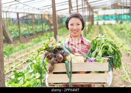 Portrait d'une agricultrice souriante tenant une caisse en bois de légumes biologiques à la ferme Banque D'Images