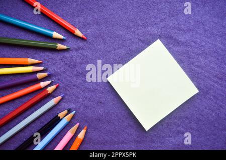 Crayons multicolores, lumineux, variables pour le dessin situé à gauche dans une spirale et un bloc-notes à droite pour votre texte sur un fond de purpl Banque D'Images