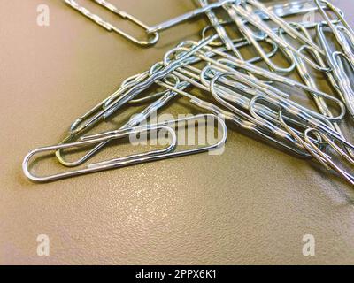 trombones en métal blanc pour conserver les documents ensemble de manière normale. articles de papeterie pour travailler avec des documents au bureau sur une table marron. Banque D'Images