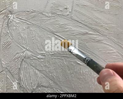 La main de l'artiste peint avec une fine brosse et une peinture volumétrique blanche sur la toile. Le processus créatif de l'art à l'école des arts Banque D'Images