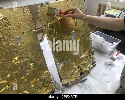 La main de l'artiste peint avec un pinceau à l'aide d'une feuille d'or jaune brillant brillant métallisé à des fins artistiques et de créativité sur toile. L'arrière Banque D'Images