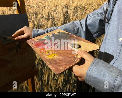 L'artiste tient un pinceau dans sa main, avec lequel il mélange des peintures aquarelles brillantes sur la palette. Le processus créatif. L'art du dessin. Insp Banque D'Images