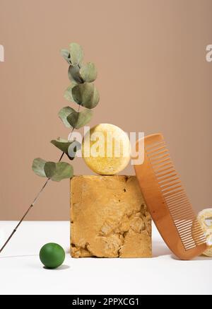Encore vie composition moderne. Barre de shampooing solide et matériaux naturels un équilibre d'idée. Peigne en bois, éponge Luffa, eucalyptus sur fond beige. Banque D'Images