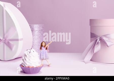 Belle petite fille en robe mignonne debout près du gâteau géant et présente des boîtes sur fond violet Banque D'Images