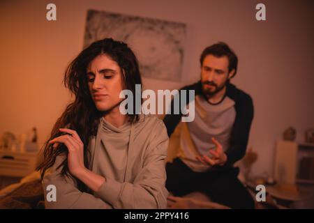 Femme mécontente assise près d'un petit ami flou quereling dans la chambre à coucher la nuit, image de stock Banque D'Images