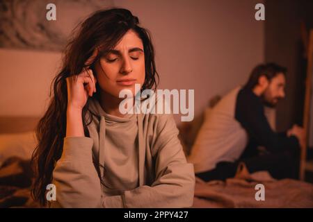 Femme mécontente assise près d'un petit ami flou sur le lit à la maison, image de stock Banque D'Images