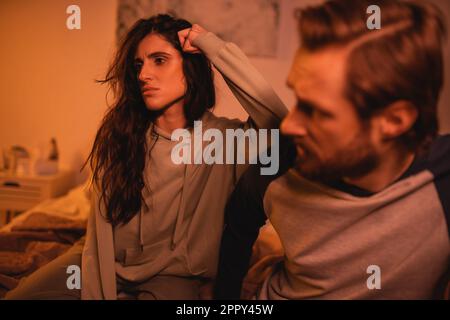 Femme pensive assise près d'un petit ami flou pendant les difficultés de relation à la maison, image de stock Banque D'Images
