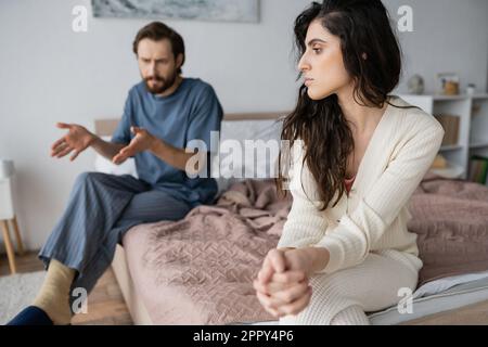 Triste femme assise près d'un petit ami furieux, en train de parler dans la chambre à coucher, image de stock Banque D'Images
