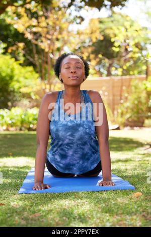 Belle jeune Black Woman fait face vers le haut chien yoga pose à l'extérieur, arbres Banque D'Images