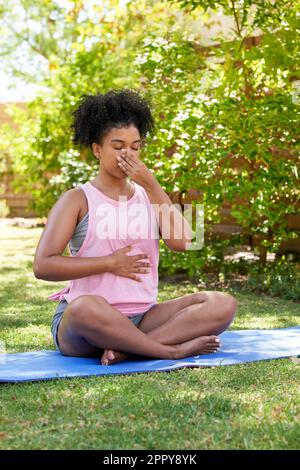 Une jeune femme multi-ethnique pratique la respiration alternée, le yoga dans le jardin Banque D'Images