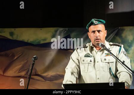 Harish, Israël. Un agent de police des frontières parle, avec un grand drapeau israélien en arrière-plan, pendant le service national de jour commémoratif, qui se tient dans tout l'État chaque année dans la veille du jour de l'indépendance d'Israël, le 4th du mois hébreu Iyar. La cérémonie a lieu pour rappeler ceux qui sont morts pendant leur service militaire ou ont été tués dans des attaques terroristes. Banque D'Images