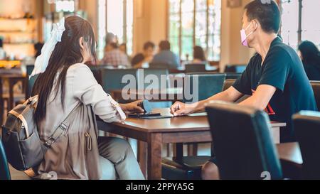 Vue arrière de la femme asiatique avec sac à dos tenant la file d'attente sans fil de la machine à appelants à la main pour attendre la nourriture dans le restaurant. Le pager d'avertissement de signal d'alarme se trouve en mode autonome Banque D'Images