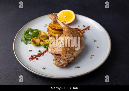 Cuisse de canard confit avec choux de Bruxelles, pommes de terre cuites au four, thym et orange. Cuisine française traditionnelle. Mise au point sélective, gros plan, arrière-plan noir. Banque D'Images