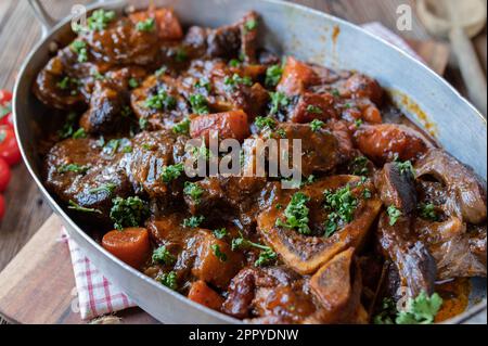 Osso bucco ou osso buco, tiges de bœuf braisées dans une rôtissoire à l'ancienne sur fond de bois Banque D'Images