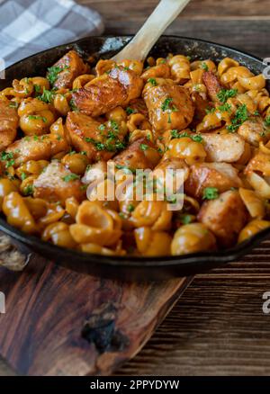 Saumon aux nouilles en coquille et sauce crémeuse à la tomate dans une casserole en fonte isolée sur une table en bois Banque D'Images