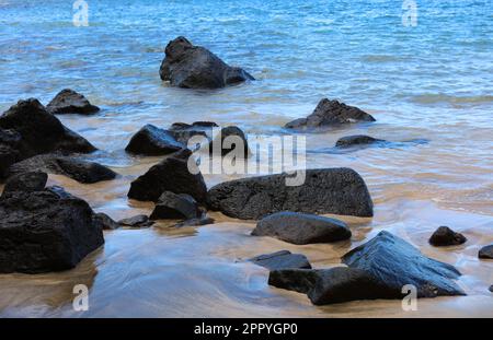 De grandes roches volcaniques noires, partiellement enterrées dans du sable noir et brun clair et dans l'océan Pacifique à Kee Beach, dans le parc national Napali Coast Wilderness Park, Kaua Banque D'Images