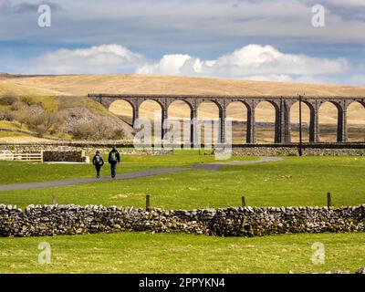 Les randonneurs qui marchent vers le viaduc emblématique de Ribblehead sur la ligne de Carlisle de Settle à la tête de Chapel-le-Dale, en dessous de Whernside, Yorkshire Dales, Royaume-Uni. Banque D'Images