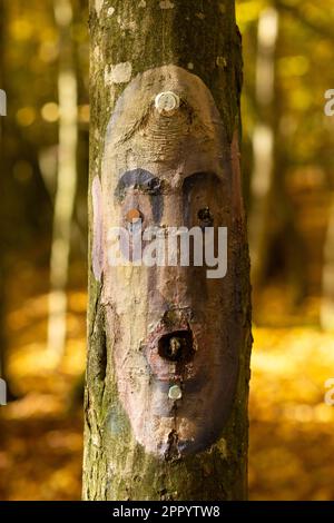 Un visage humain triste sous la forme d'une icône est peint sur le tronc d'un arbre. Fond de bokeh défoqué, tous dans des tons pastel, dans une forêt pleine de jour l Banque D'Images