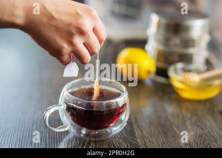 La femme met le sac de thé dans la tasse en verre avec de l'eau chaude Banque D'Images