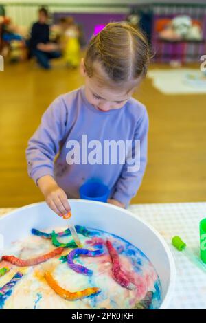 Une petite fille goutte de l'eau sur des vers de papier colorés. Le développement sensoriel et les expériences, les activités thématiques avec les enfants, les compétences moteur fine Banque D'Images