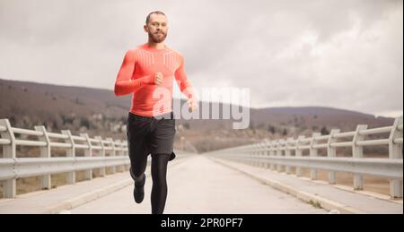 Un homme barbu dans des vêtements de sport qui traverse un pont par une journée nuageux Banque D'Images