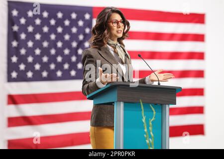 Jeune femme sur un piédestal donnant un discours et faisant des gestes avec les mains avec le drapeau des États-Unis en arrière-plan Banque D'Images